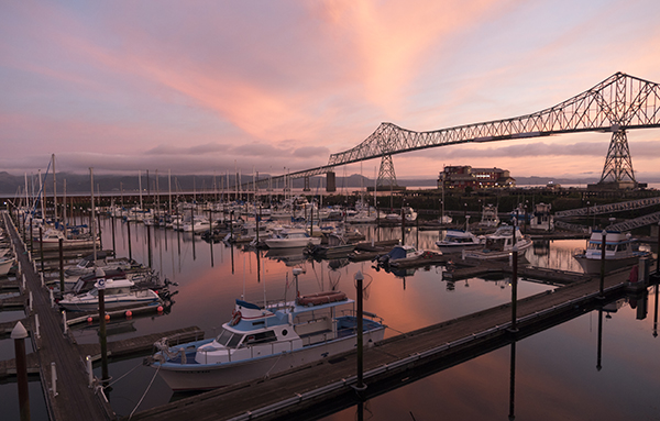 Large metal bridge connecting Washington and Oregon at sunset, with pleasure boat marina in the foreground.